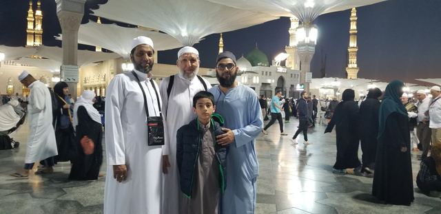 Amity travelers and a boy at night in the courtyard of Masjid an-Nabawi under the umbrellas