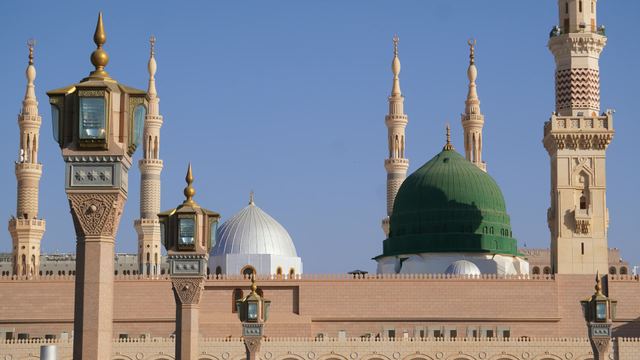 The Green Dome and minarets of Masjid an-Nabawi in Madinah against a clear blue sky.