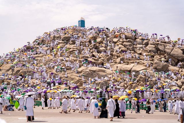 Pilgrims in white with colorful umbrellas covering the rocky slopes of Jabal al-Rahmah at Arafat.