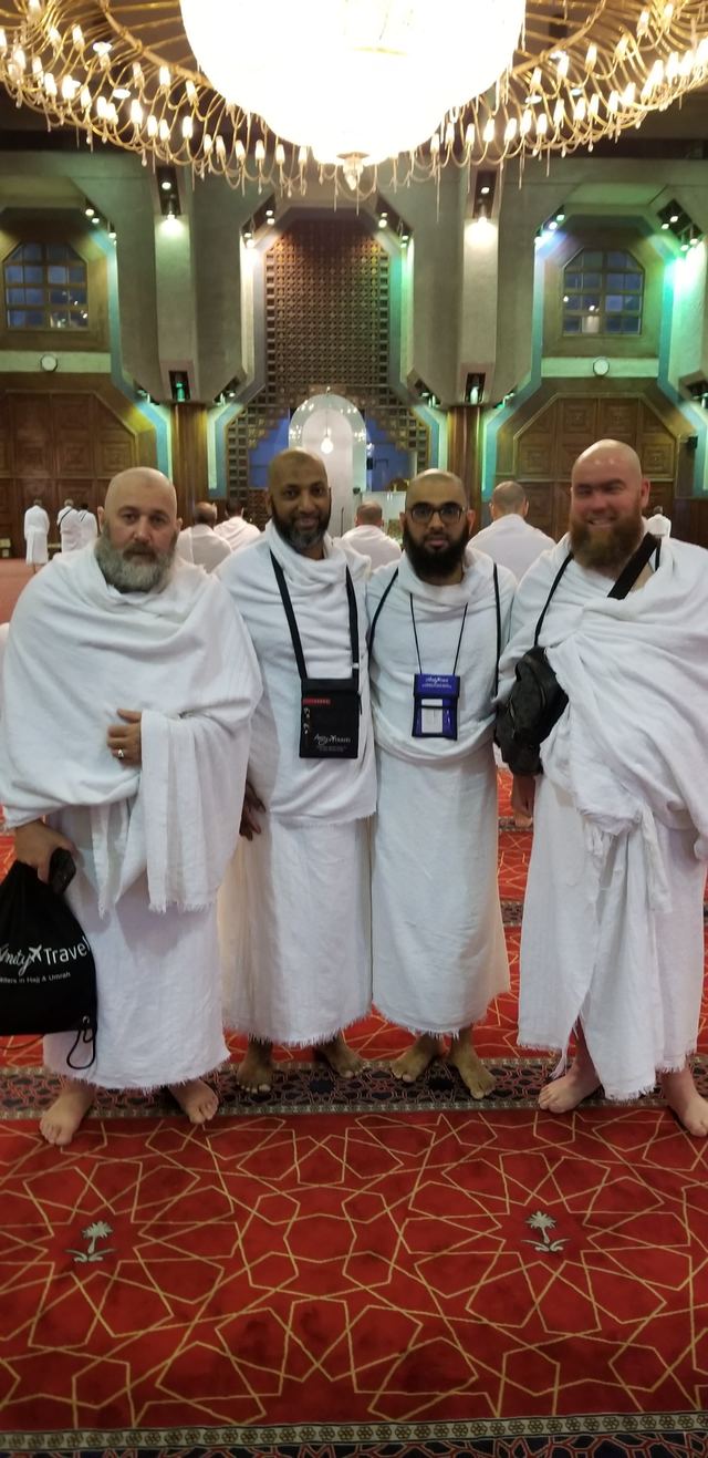 Four Amity travelers in ihram inside a mosque with a large chandelier