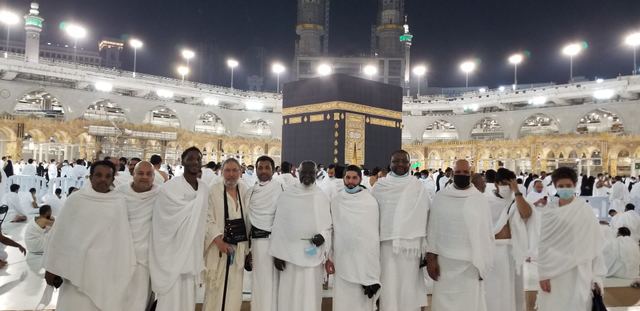 Amity Umrah group in ihram standing together in front of the Ka‘bah at night