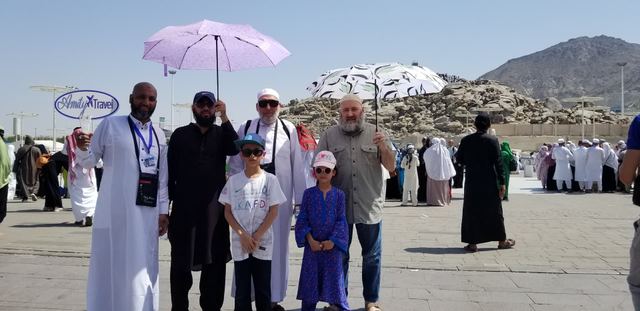 Amity travelers with umbrellas at Arafat, Jabal al-Rahmah behind, Amity sign at left