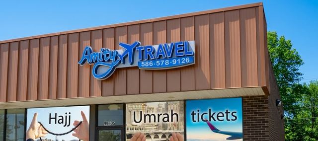 The Amity Travel office storefront: the blue logo sign above windows with Hajj, Umrah and tickets posters.