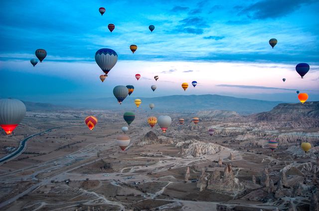 Hot-air balloons rising over the valleys of Cappadocia under a blue sky.